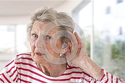 Elderly lady with hearing problems due to ageing holding her hand to her ear as she struggles to hear, profile view on Stock Photo