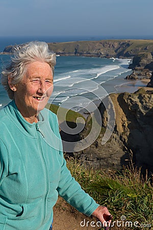 Elderly lady in her eighties with walking stick by beautiful coast scene with wind blowing through her hair Stock Photo