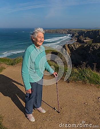 Elderly lady in her eighties with walking stick by beautiful coast scene with wind blowing through her hair Stock Photo