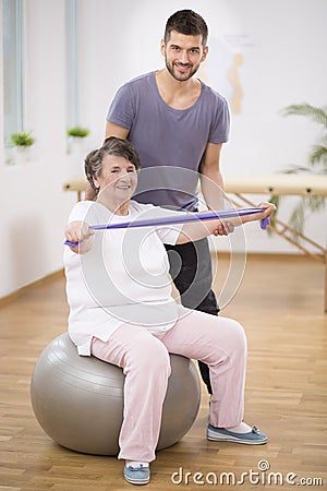 Elderly siting on the exercise ball during physiotherapy with her young instructor Stock Photo