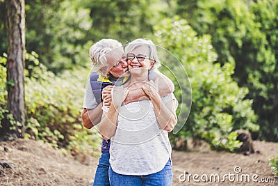 Elderly lifestyle people with couple of caucasian active senior kissing in relationship with green plants nature in background - Stock Photo
