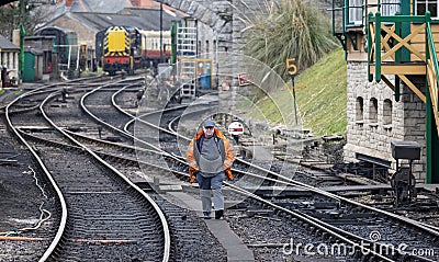 Elderly male volunteer at the Swanage steam railway walking on the tracks by the signal box at Swanage station, Dorset, UK Editorial Stock Photo