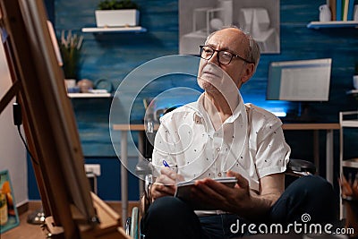 Elderly man artist living with disability doing sketch on notebook for practice before drawing on easel Stock Photo