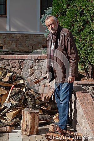 Elderly man in jacket stands in front of pile firewood Stock Photo