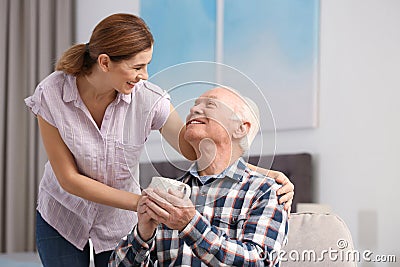 Elderly man with cup of tea near female caregiver at home. Stock Photo