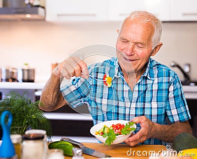 elderly man eating fresh vegetable salad at home Stock Photo