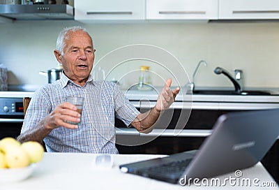 Elderly man with glass of wine communicates virtually using a laptop and the Internet Stock Photo