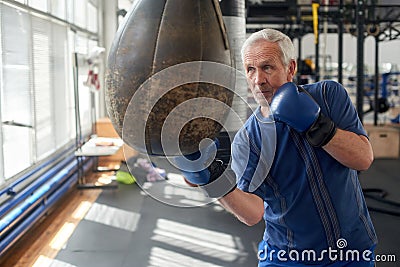 Elderly man hitting punching bag in boxing studio. Stock Photo