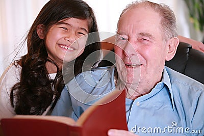 Elderly man and little girl reading Bible together Stock Photo