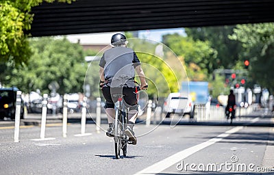 An elderly man rides a bicycle on a dedicated bike path along a city street Editorial Stock Photo