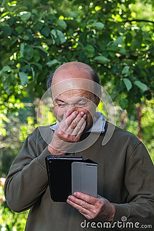 Elderly man with a runny nose looking for cure on the Internet Stock Photo