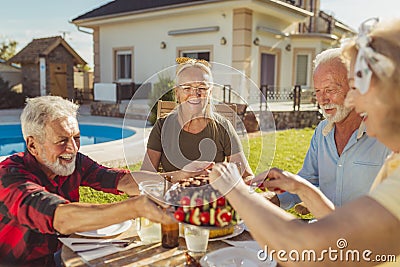 Elderly man serving food on a tray while having lunch with friends in the backyard Stock Photo