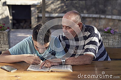 A elderly man sitting doing crosswords hobby with his grandson Stock Photo