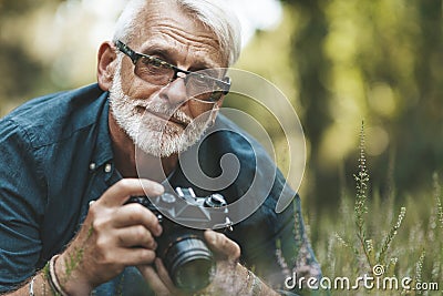 Elderly man takes pictures of flowers in park, pensioner on walk. Active hobby of mature person Stock Photo