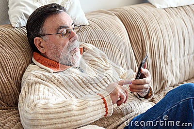 Elderly Man Using Cellphone Sitting On Sofa At Home, during Coronavirus quarantine. Stock Photo