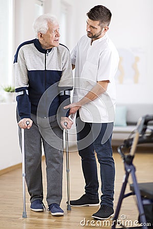 Elderly man walking on crutches and a helpful male nurse supporting him Stock Photo