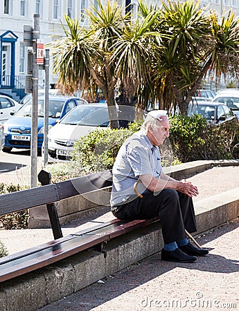 Elderly man wearing a knotted handkerchief on top of his head sitting down on wooden bench Editorial Stock Photo