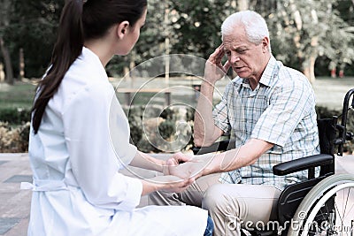 An elderly man in a wheelchair complains of a headache to a doctor Stock Photo