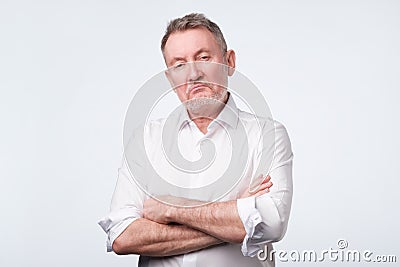 Elderly man in white shirt with his arms crossed looking depressed and annoyed Stock Photo