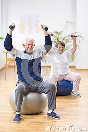 Elderly man and woman exercising on gymnastic balls during physiotherapy session at hospital Stock Photo