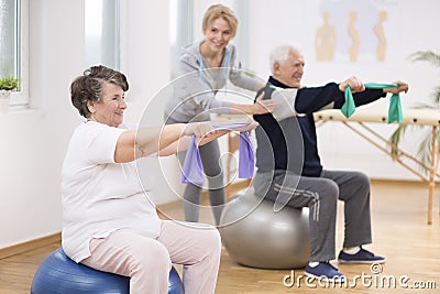 Elderly man and woman exercising on gymnastic balls during physiotherapy session at hospital Stock Photo