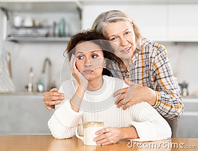 Elderly mother calms her daughter down and asks her for forgiveness after a domestic quarrel in kitchen Stock Photo