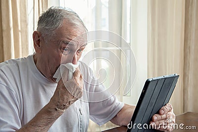 Elderly person with allergies and colds coughs and sneezes into a napkin. A sick old man makes purchases online while at home Stock Photo