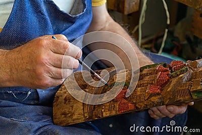 Elderly repairman painting with paintbrush on a small business a woodwork. Senior artisan with big hand painting artwork. Stock Photo
