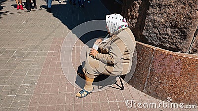 Elderly sad woman begging money while sitting on a stool in Kreschatik street in Kiev Editorial Stock Photo