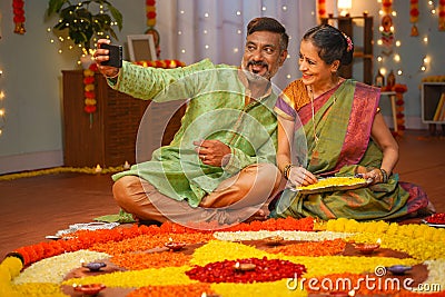 elderly senior couple taking selfie during diwali festive preparation at home in front of flower rangoli - concept of Stock Photo