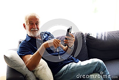 Senior man sitting alone and playing mobile phone at home. Stock Photo