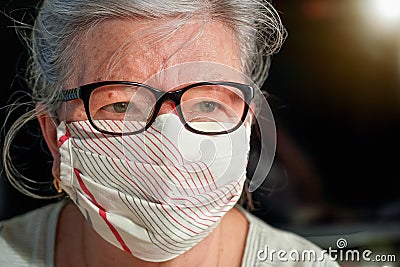 Elderly senior woman with glasses wearing hand made cotton mouth nose virus face mask. Coronavirus covid19 outbreak prevention Stock Photo