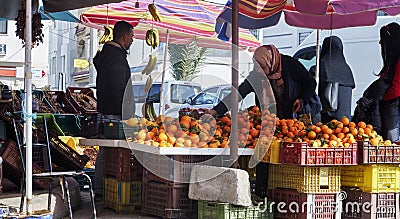 Elderly Tunisian woman wearing a headscarf checks the oranges at a fruit stall Editorial Stock Photo