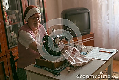 Elderly white woman with wrinkled hands and face works on a sewing machine at home. concept is elderly people Stock Photo