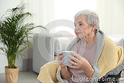 Elderly woman covered with blanket drinking tea at nursing home. Assisting senior people Stock Photo