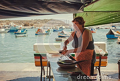 Elderly woman cutting fresh sea fish on street market of the sunny fishing town Editorial Stock Photo