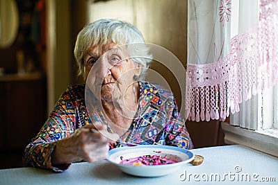 An elderly woman eating soup sitting at a table. Stock Photo
