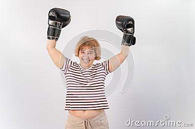 An elderly woman in fighting gloves raises her hands up on a white background. Victory in a duel Stock Photo