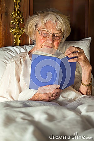 Elderly woman in her nightgown reading in bed Stock Photo