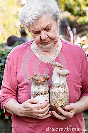 Elderly woman holding home cultivated mushrooms, selfmade fungiculture on glasses Stock Photo