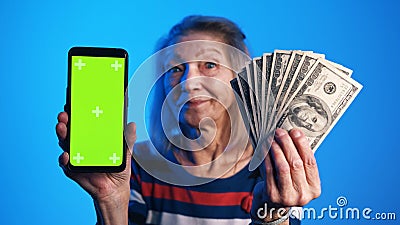 Elderly woman holding phone with green screen in one and money in another hand. Lottery win Stock Photo