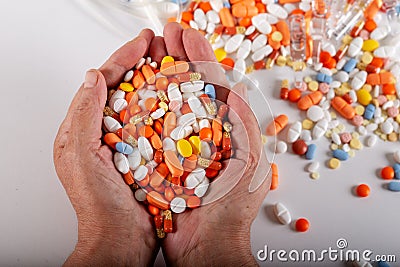 An elderly woman holds a lots of colored pills in hands on a white background. Stock Photo