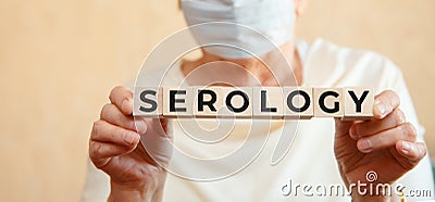 Elderly woman holds wooden cubes in her hands with the inscription SEROLOGY Stock Photo