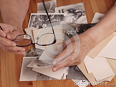 An elderly woman looks at old photographs, recalls her past youth. Hands on the table. Loneliness,, memories Stock Photo