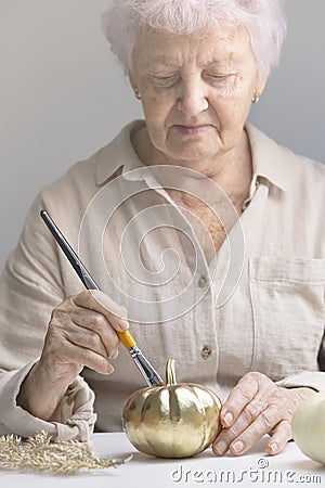 An elderly woman paints a pumpkin. Lifestyle pensioners. Old hands paint pumpkin with gold paint with brush Stock Photo