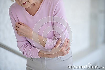 Elderly woman in pink shirt suffering from pain in elbow Stock Photo