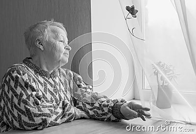 Elderly woman sits and looks out the window. Stock Photo