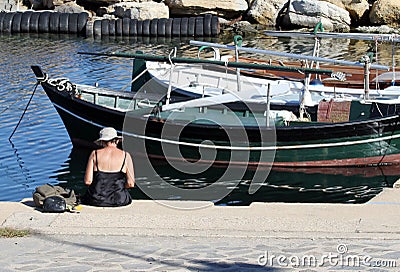 Elderly woman sitting on the pier. Boats in the background. Editorial Stock Photo