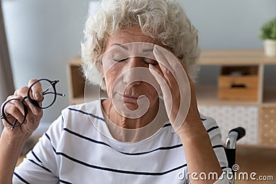 Elderly woman sitting in wheelchair taking off glasses reduces eyestrain Stock Photo