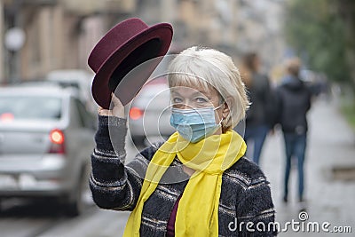 An elderly woman 60-65 years old greets holding up a fashionable hat on the background of the city landscape. Concept: retirement, Stock Photo